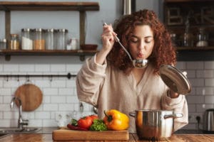 A young woman blows the steam off a ladle as she tries one of her favorite winter soup recipes.