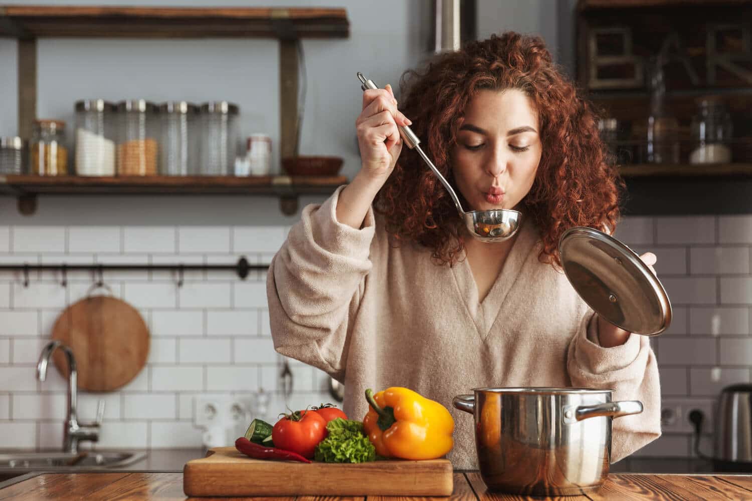 A young woman blows the steam off a ladle as she tries one of her favorite winter soup recipes.